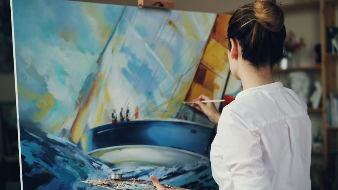 A woman paints a blue ship on canvas.