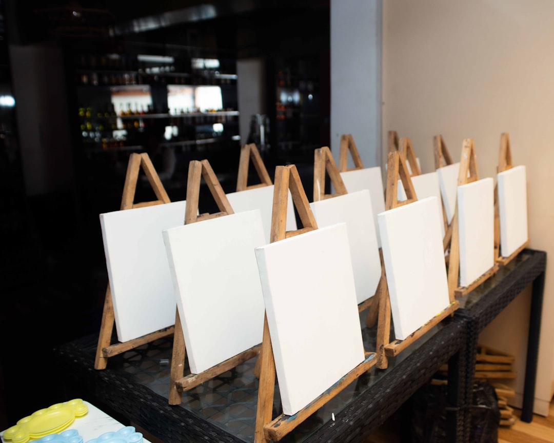 White canvases on wooden easels lined up indoors.